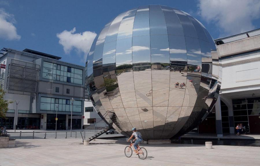 Large, reflective globe in a city space with cyclist out front