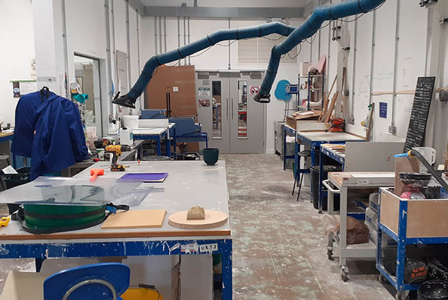 A workshop with large tables, various sculpting materials and shelves.