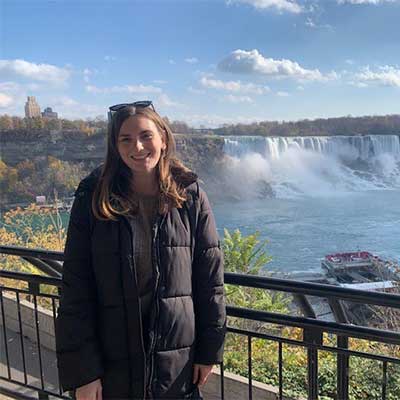 Person in black coat and long hair standing in front of a waterfall