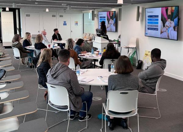 People sitting together at round tables watching someone give a power point presentation