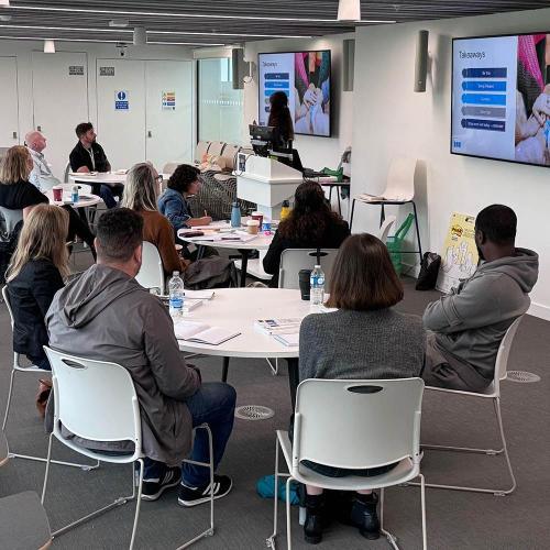 People sitting together at round tables watching someone give a power point presentation