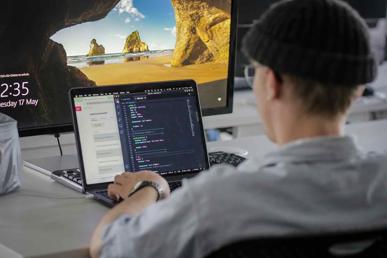 Person in hat in front of laptop and monitor