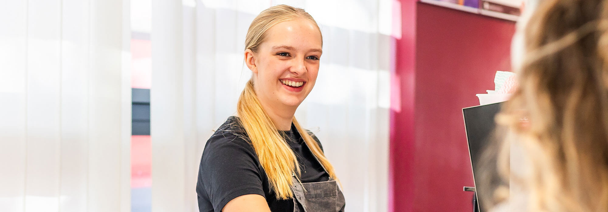 Smiling woman wearing an apron passes a cup of coffee to a colleague over a counter