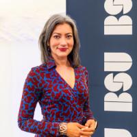 Person with dark hair standing in front of BSU board in a blue and orange patterned dress
