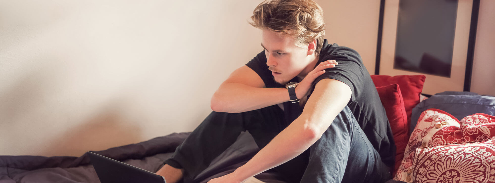 Young man sitting on bed using a laptop