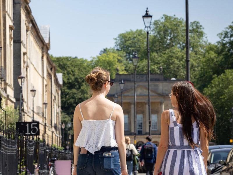 Two students walking down Bath's historical streets in the sunshine