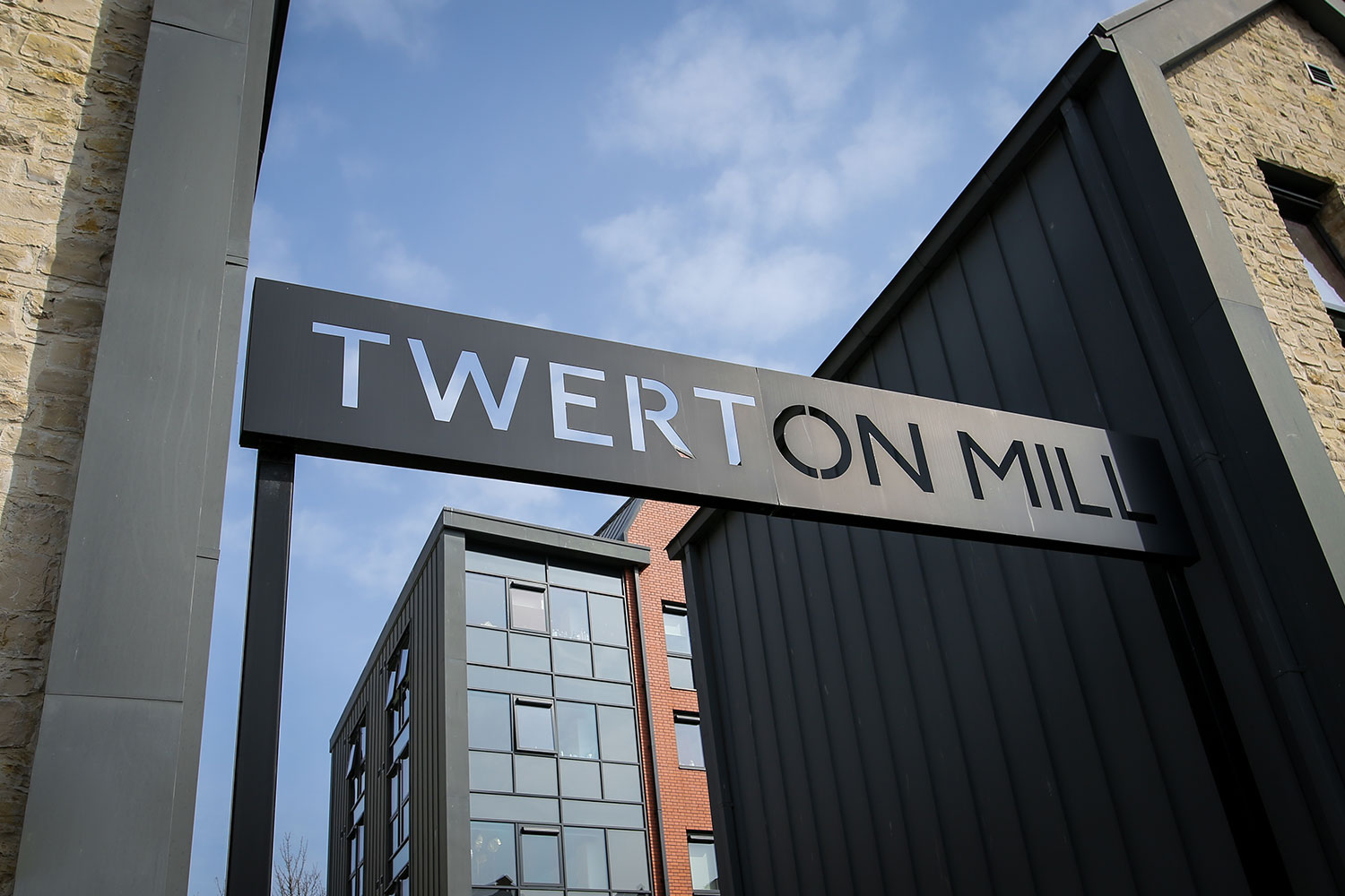 Exterior of a modern stone building with a metal sign for Twerton Mill