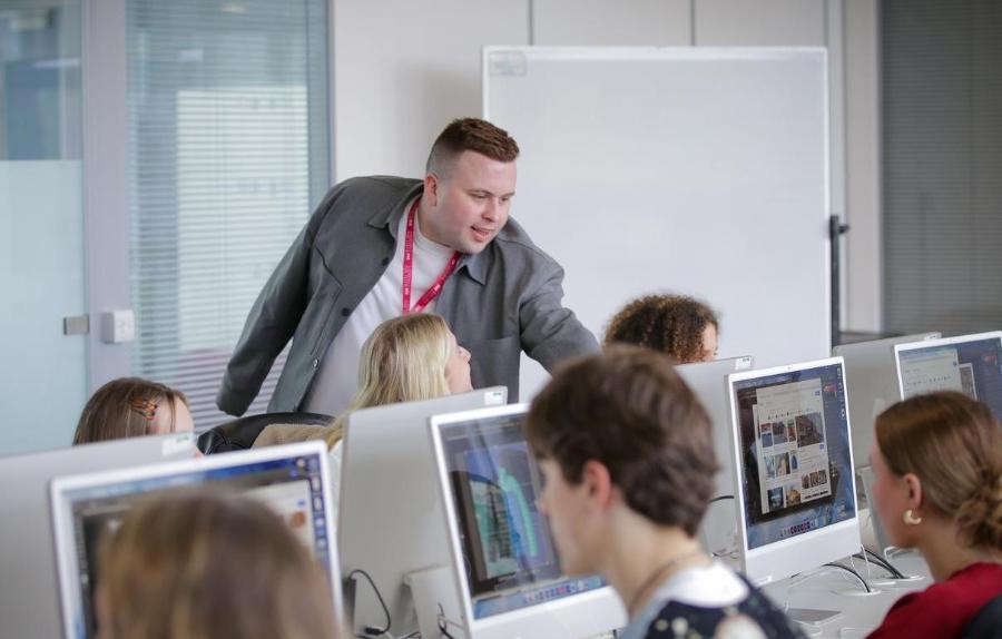 Man in a grey suit in a computer lab looking at the screens.