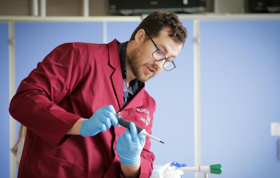 Man in a red lab coat holding a pipette.