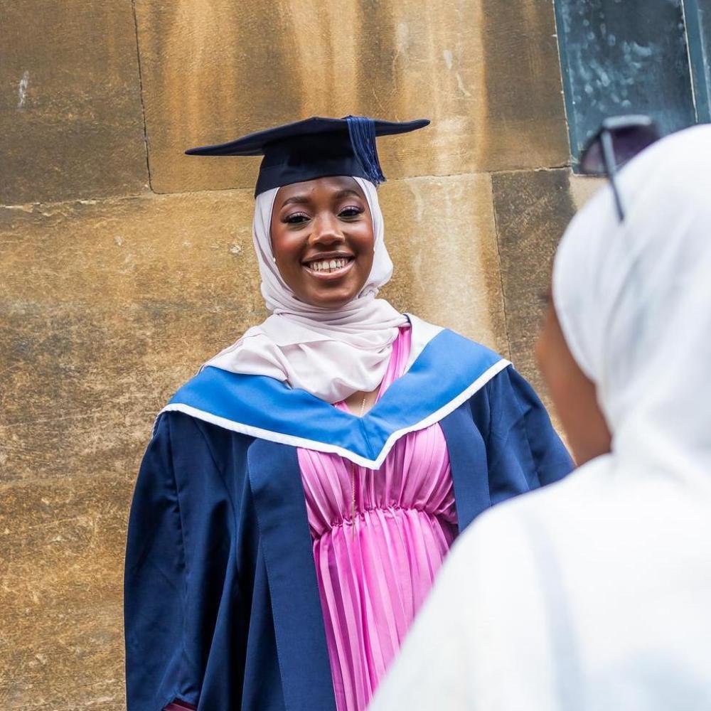 Young black woman in modest dress wearing a graduation robe and cap.