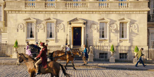 An exterior of a house in the Royal Crescent. In front of the building are actors dressed in regency clothing and riding horses.