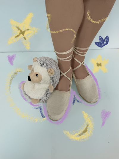 A pair of feet in ballet shoes, with a toy stuffed hedgehog