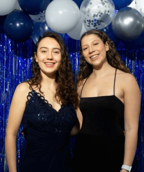 Two students stand smiling wearing formal dresses