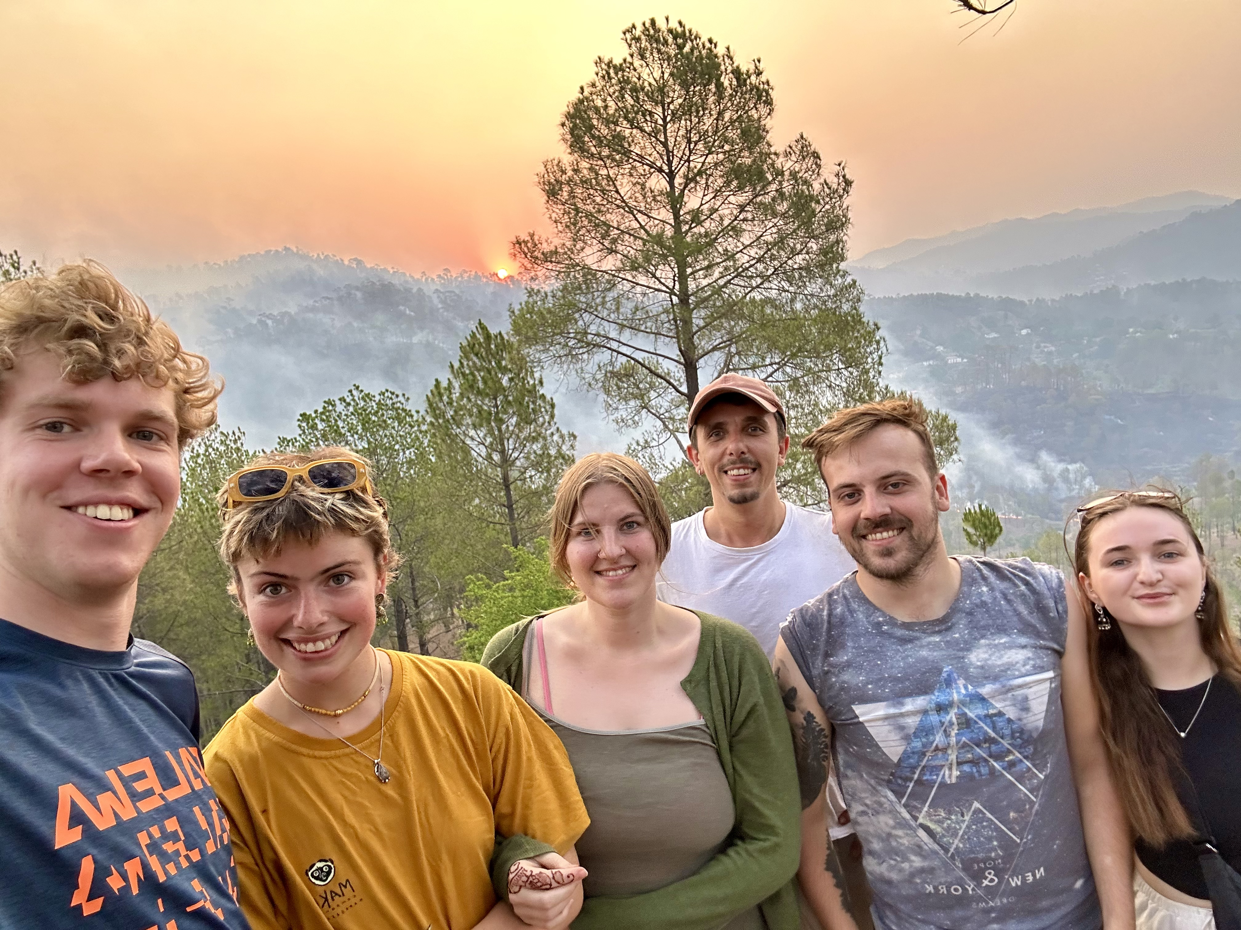 Group of young people smiling with sun setting over mountains in the background