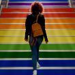 Person with a backpack and red-dyed curls walking up stairs decorated with a rainbow of pride colours