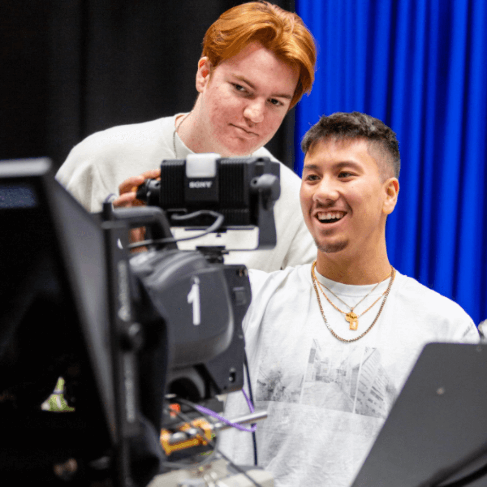 Two students smile whilst operating a camera.