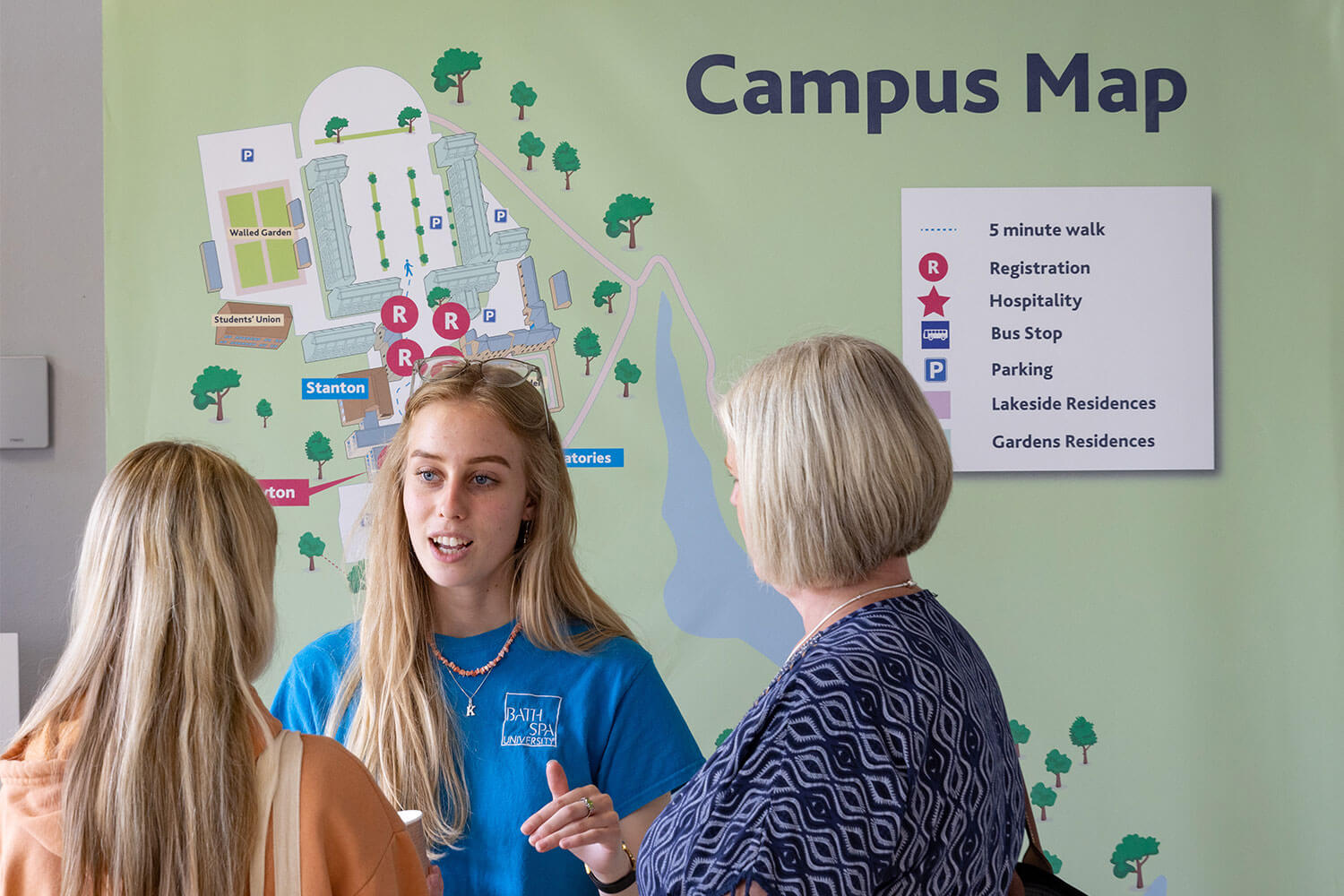 A student ambassador talks to visitors to the university in front of a map of the campus