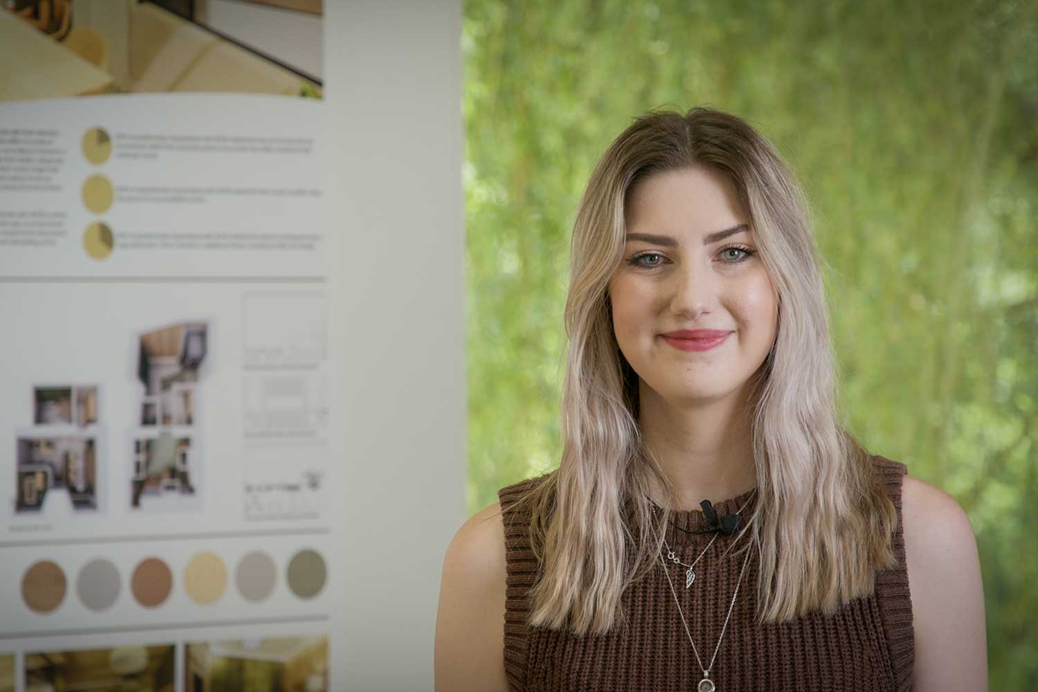 A student with long hair stands in front of her degree show exhibition