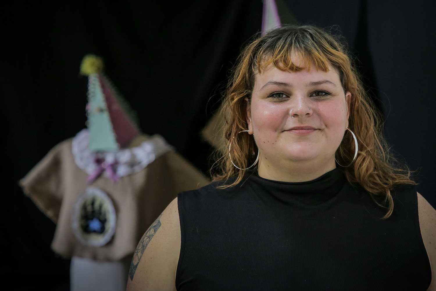 A student with shoulder-length hair stands in front of items from their degree show exhibition