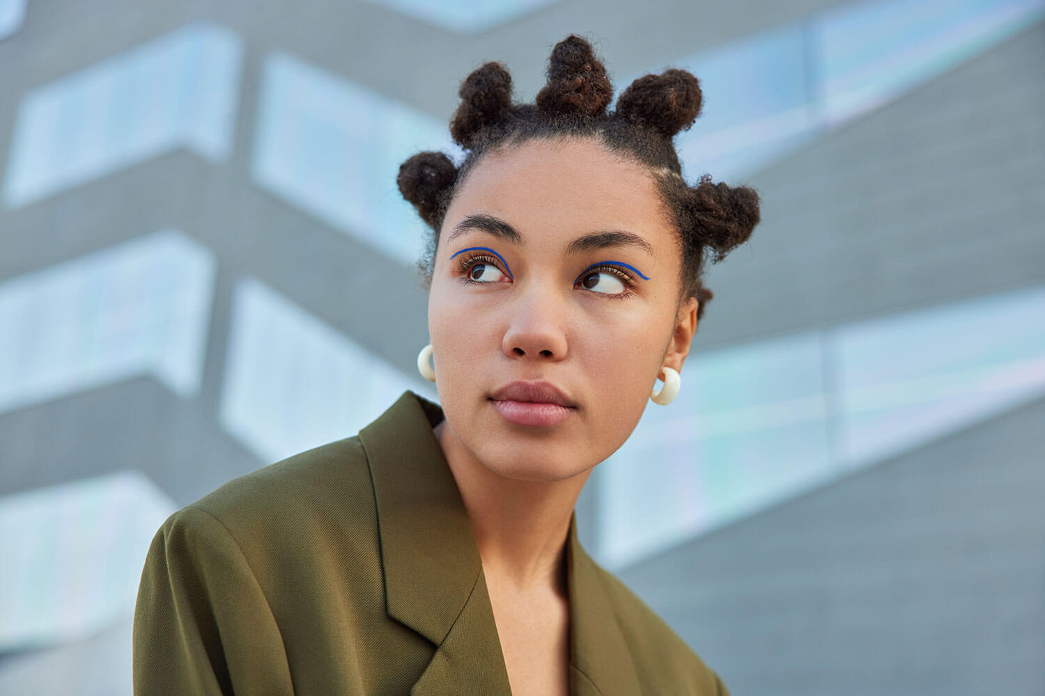 Stylish woman with hair buns poses against blurred background