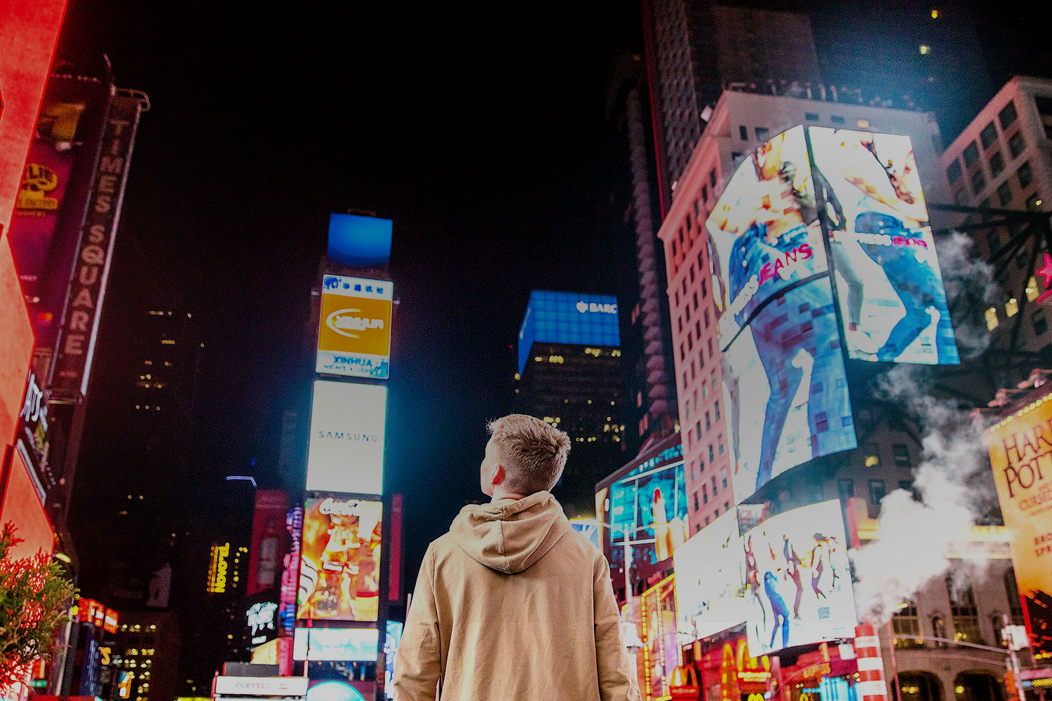 Young person in a beige hoodie looking at screens in Times Square