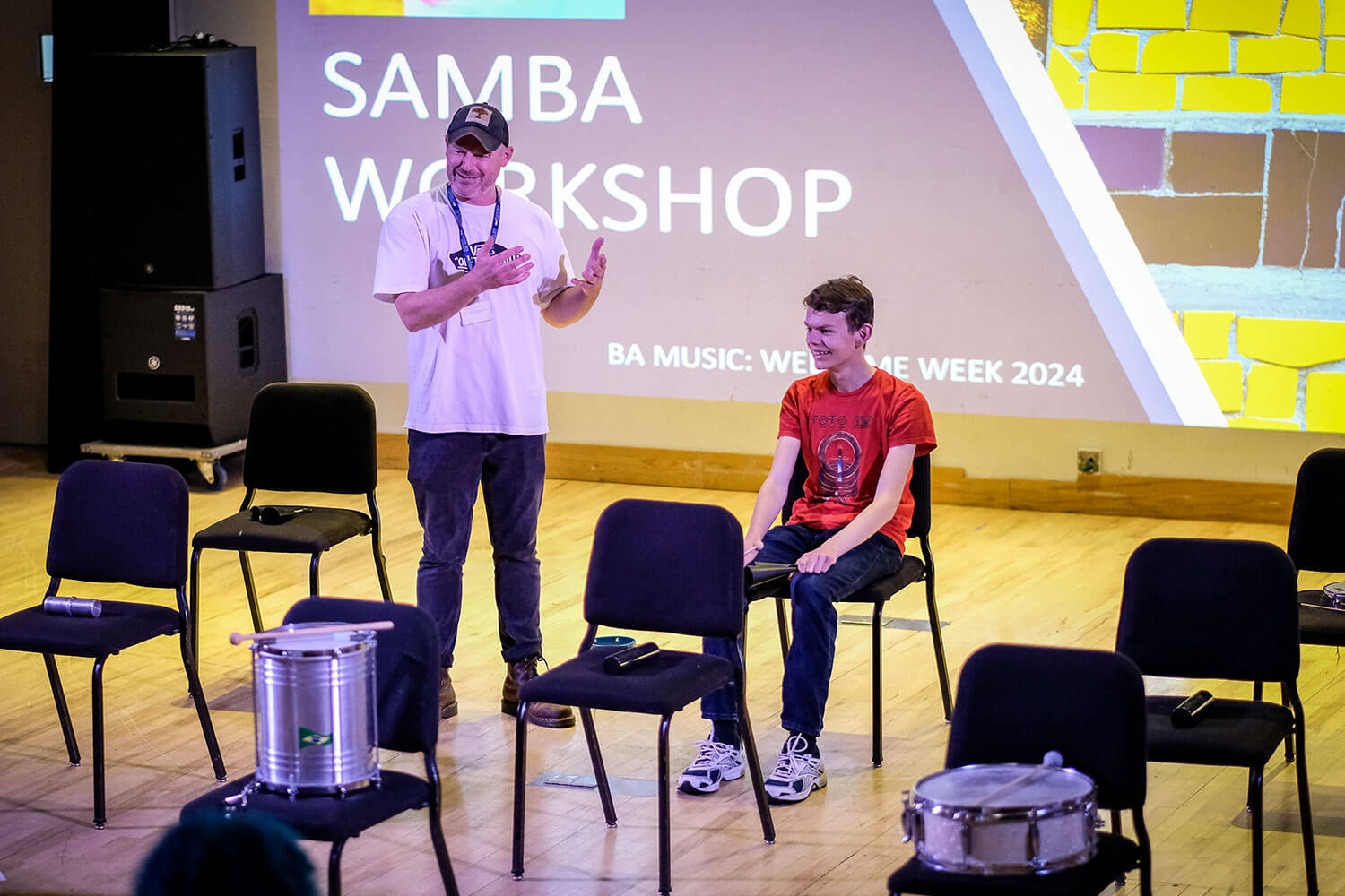 Student with a tutor taking part in a Samba workshop where various instruments are laid out for students to use