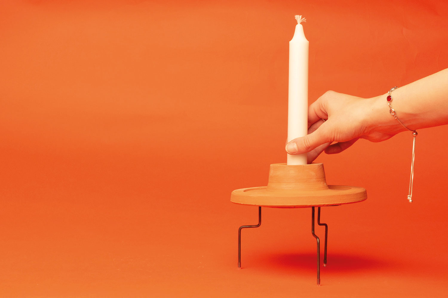 A hand places a white candle into an orange candle stick holder.