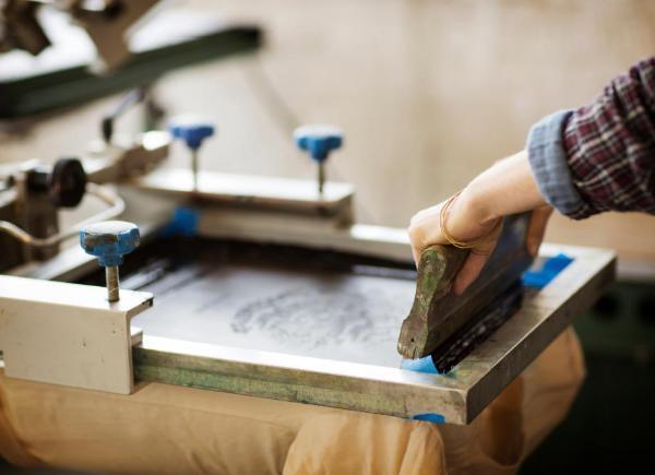 An over the shoulder shot of two hands screen printing. 