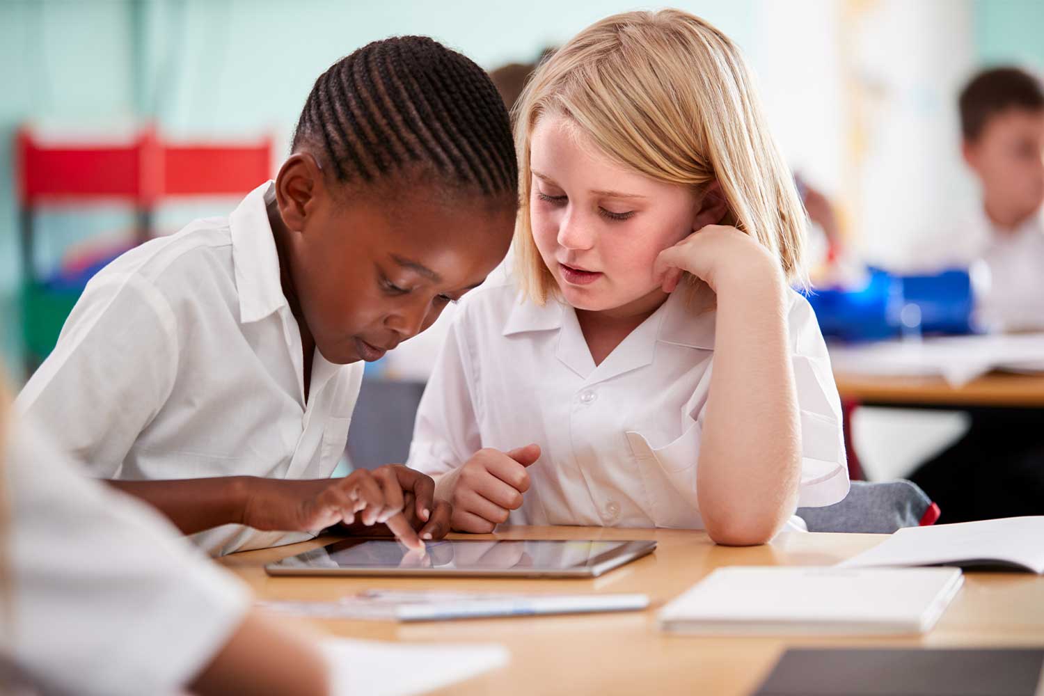 Two young pupils in uniform in a classroom setting working on a tablet