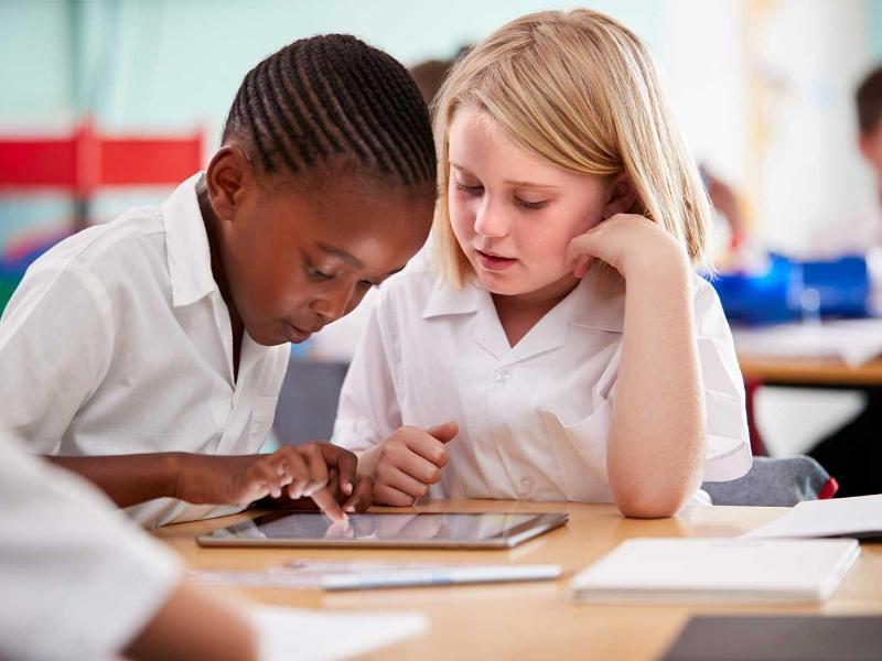 Two young pupils in uniform in a classroom setting working on a tablet