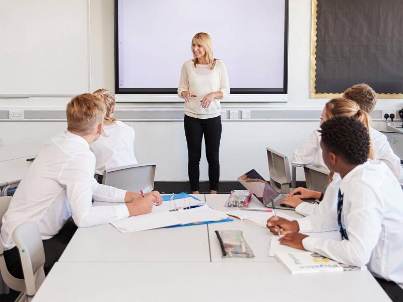 Teacher standing next to interactive whiteboard and teaching lesson to pupils