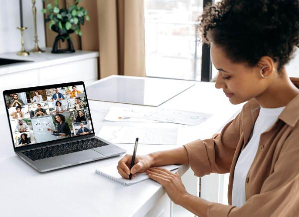 A woman writing on paper while a webinar plays in the background