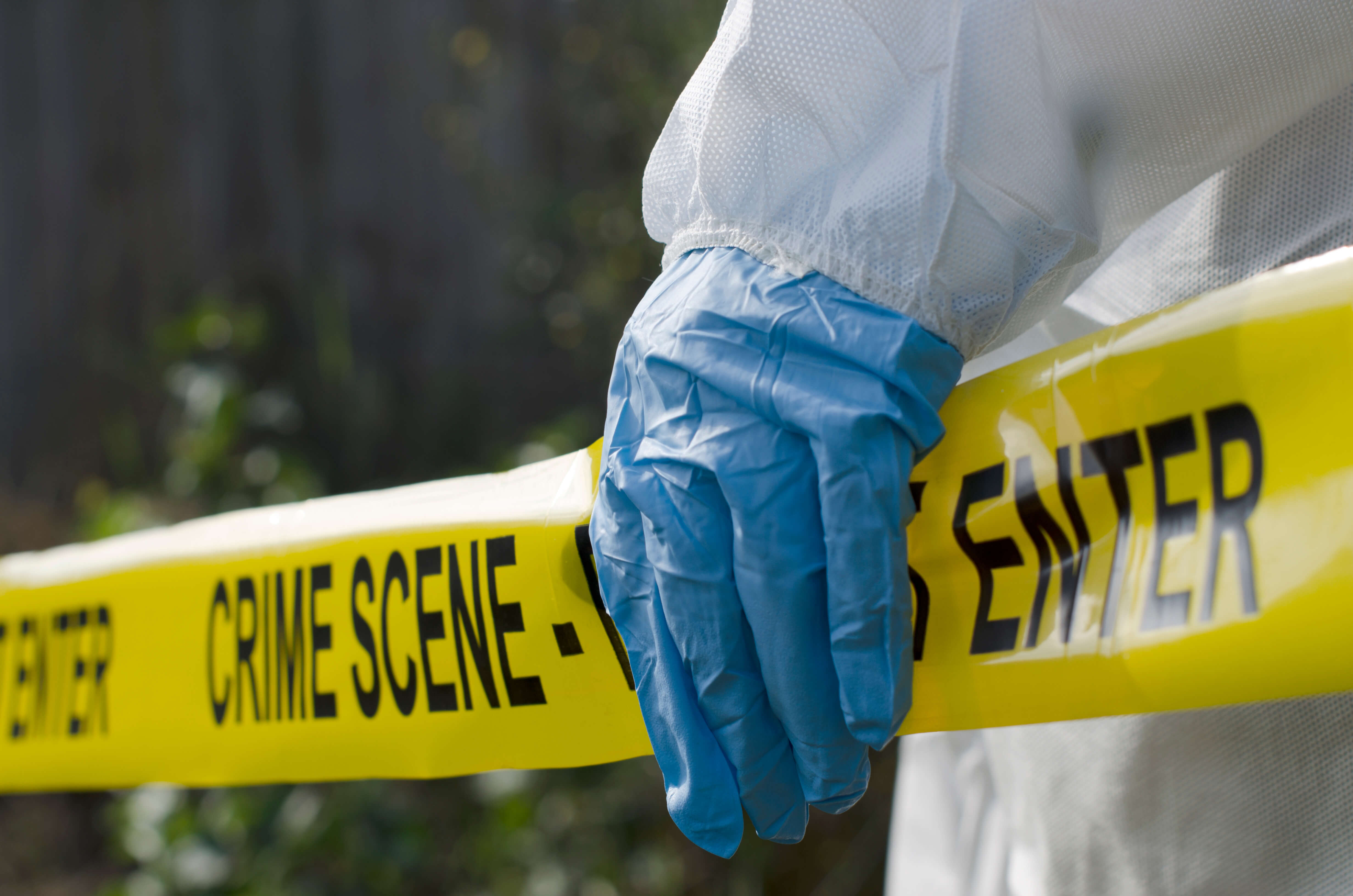 A blue gloved hand holds on to yellow crime scene investigation tape