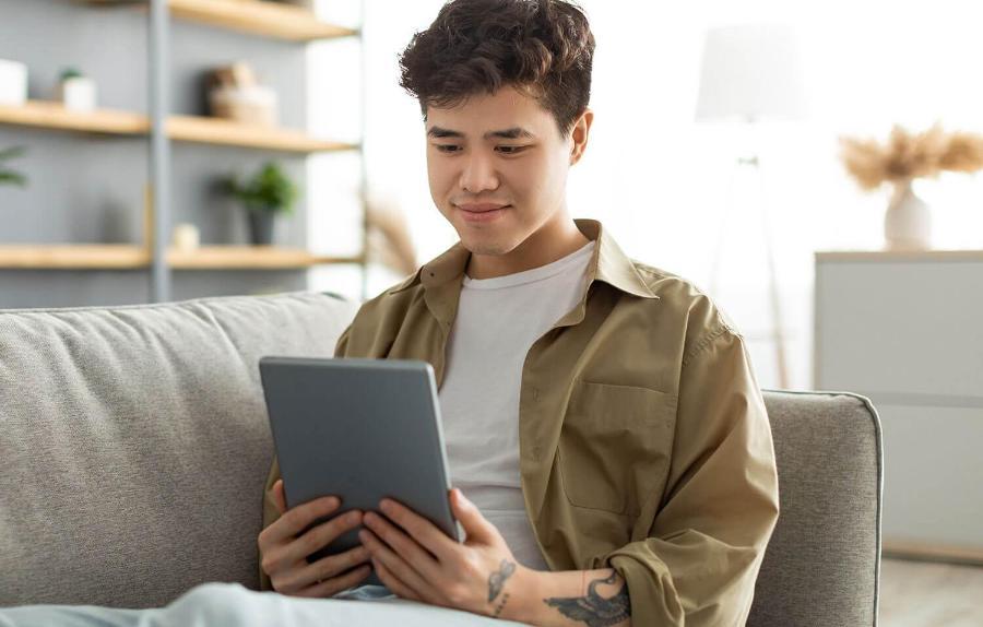 Young man with tattoos uses a tablet while sitting on a sofa