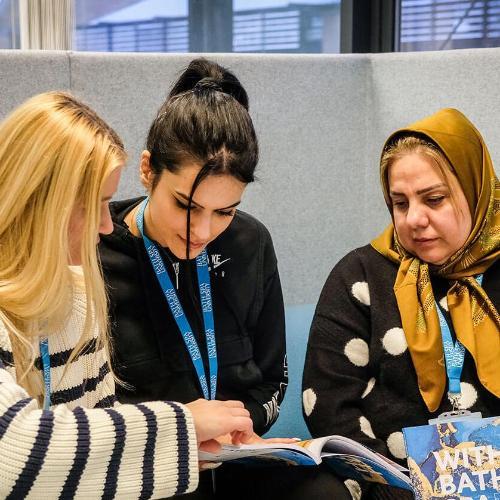 Three female presenting staff with booklets sitting in a booth