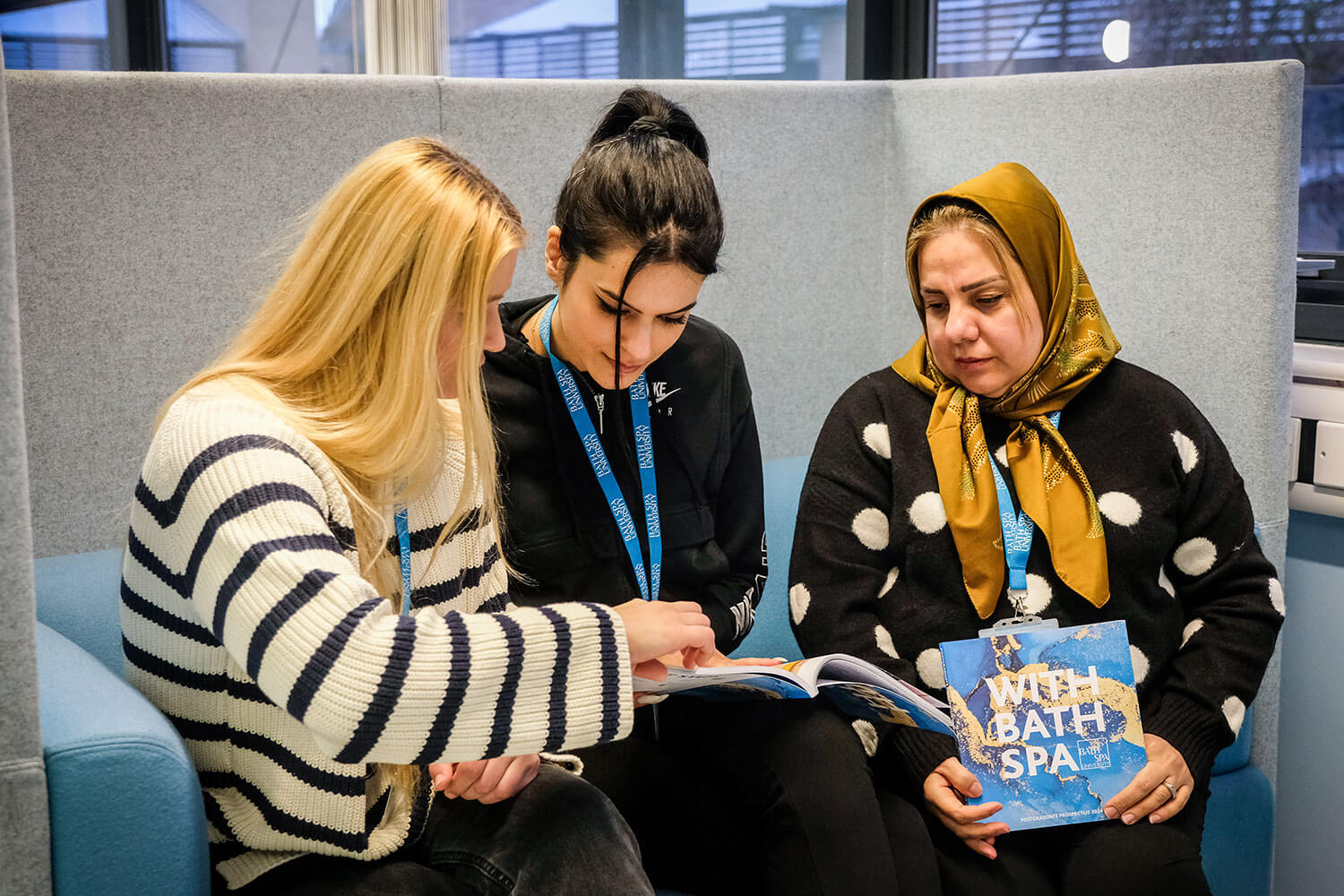 Three female presenting staff with booklets sitting in a booth