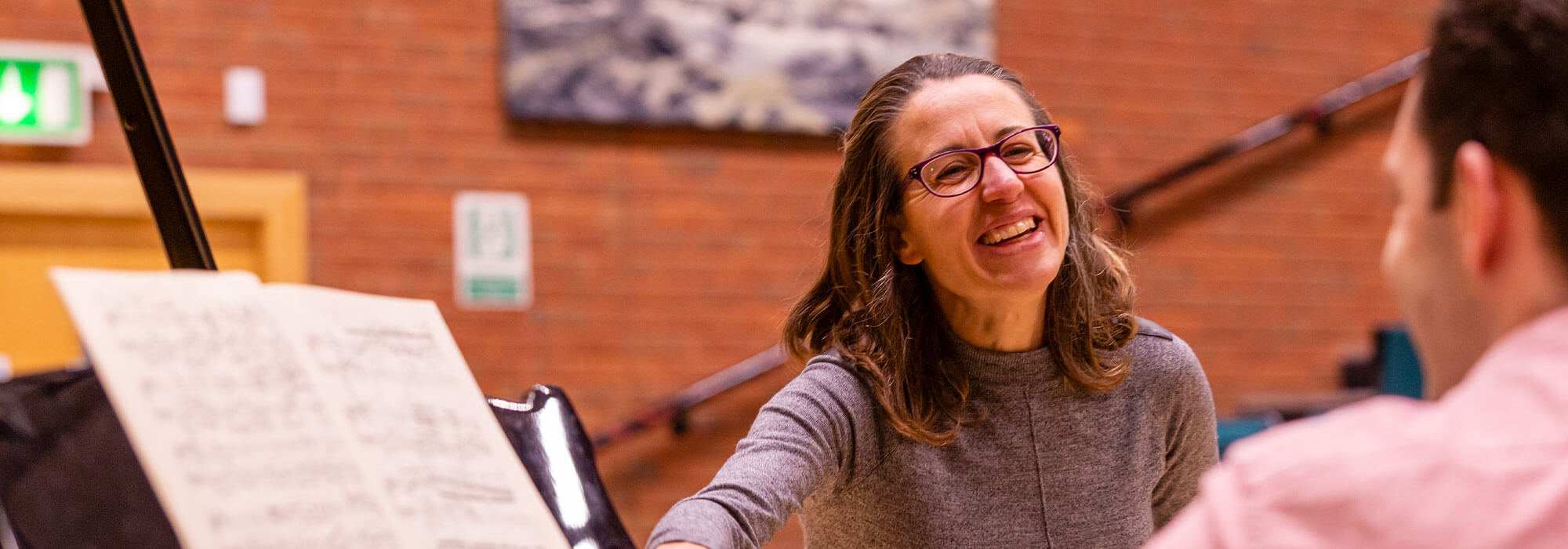 Smiling female tutor talks to a student who is sitting at a piano