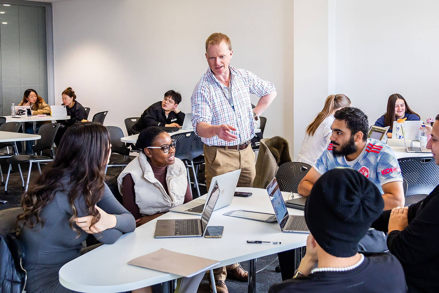 Male tutor in a checked shirt talks to a group of students taking part in a seminar discussion