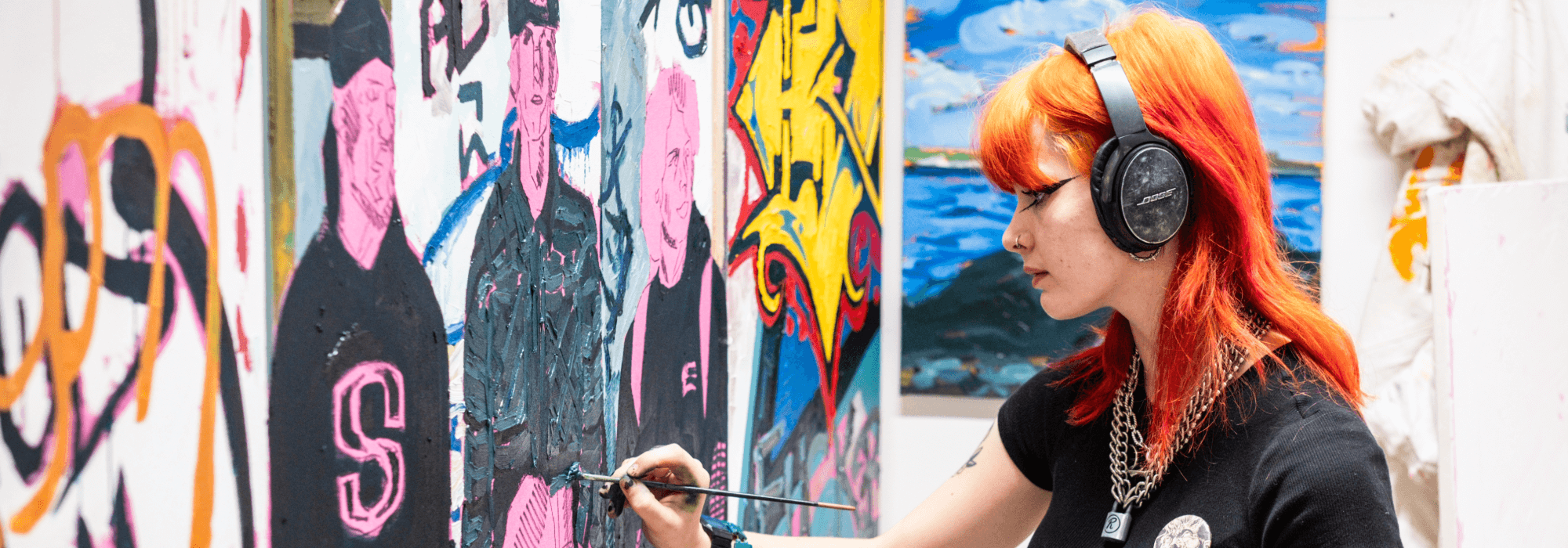 A student with bright hair paints a large mural.