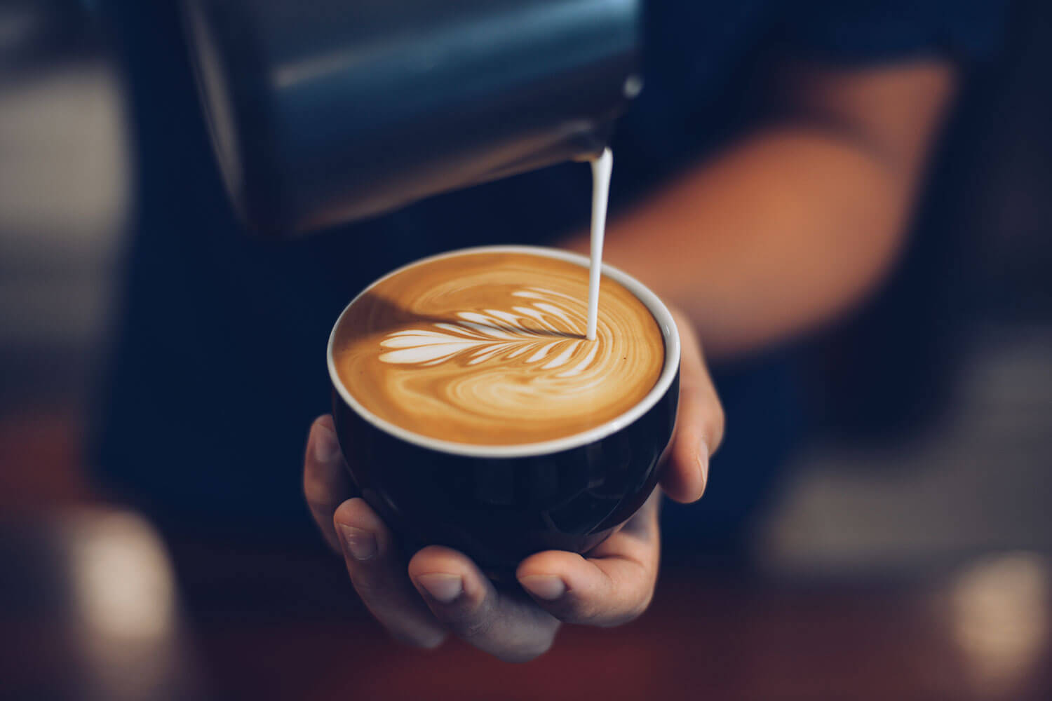 Barista pouring milk into a mug of coffee