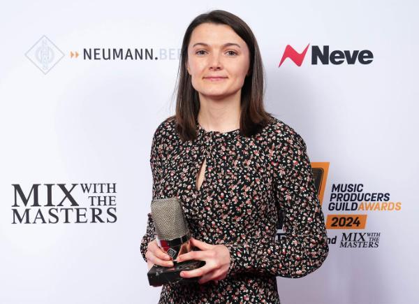 A student stood in front of an advertising stand holding a trophy shaped like a microphone