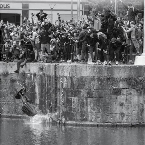 A black and white photo of protesters throwing a statue of Edward Colston in the harbour in Bristol