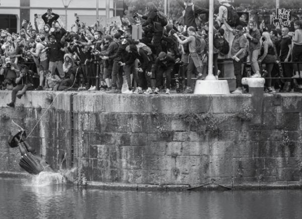 A black and white photo of protesters throwing a statue of Edward Colston in the harbour in Bristol