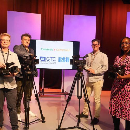 Four people stood in front of a screen, with two cameras in front of them, both on tripods