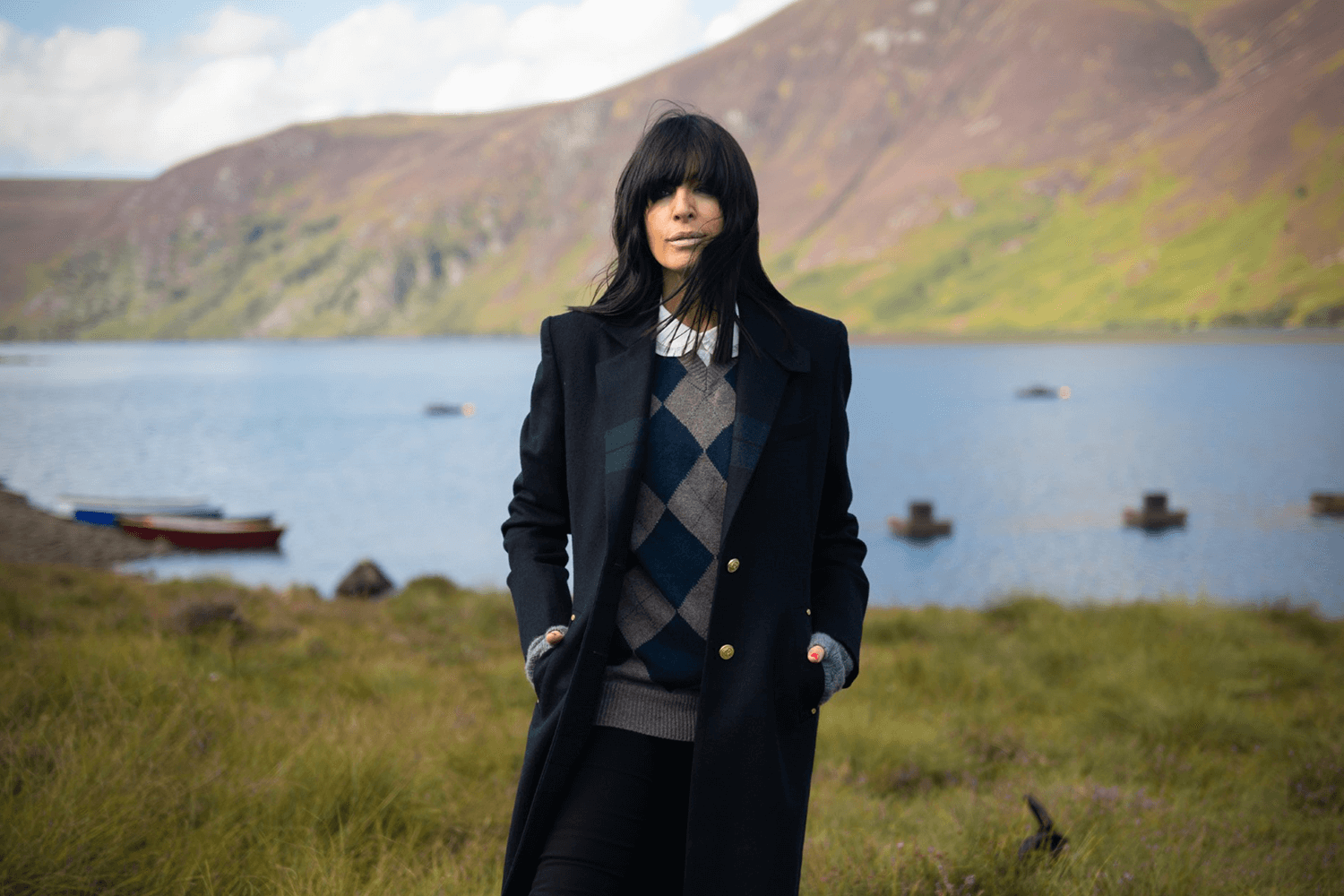 Claudia Winkleman stands in the countryside, looking at the camera.