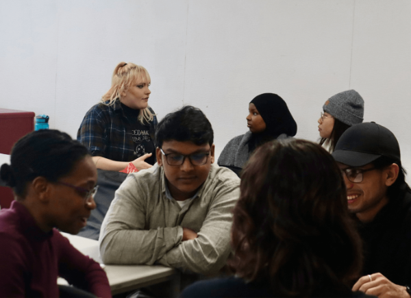 A group of students sit around two tables talking to each other