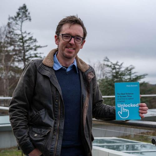 person stands on a balcony holding up a book