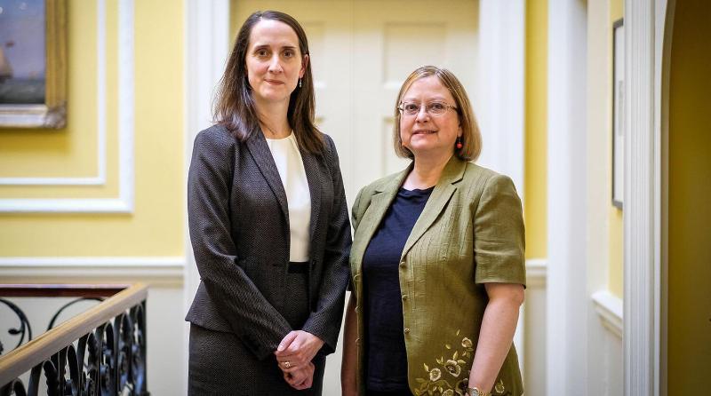 Two women in smart clothing stand together smiling