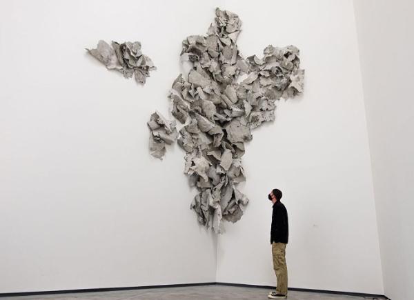 A person looking up at abstract art installation on wall above 
