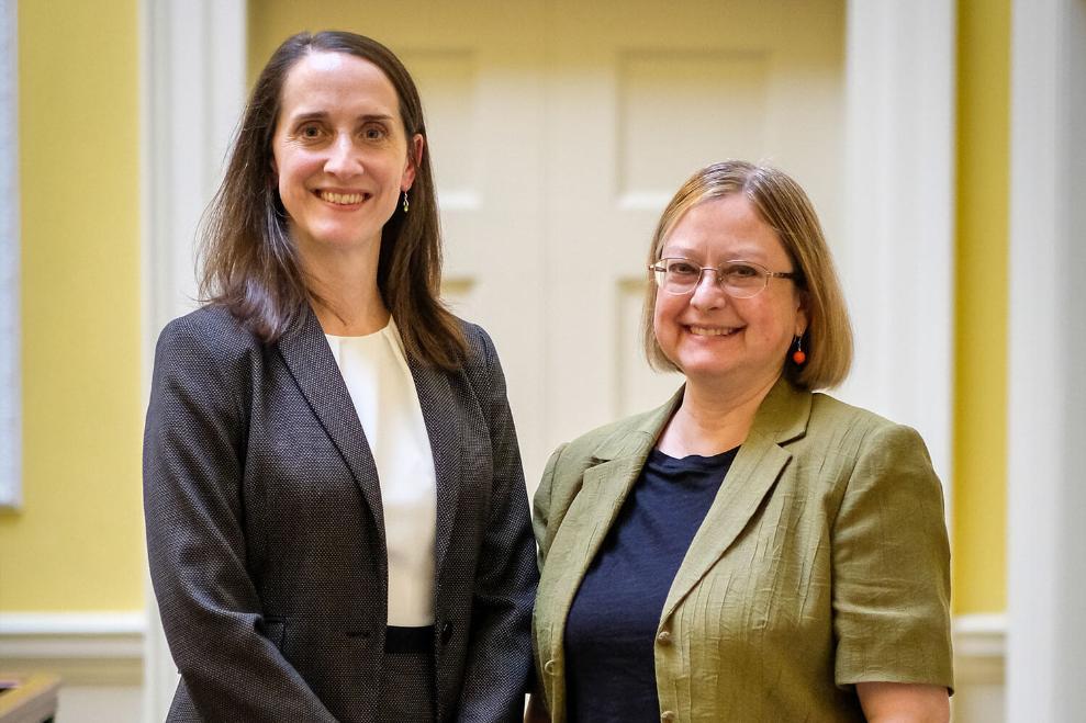 Two women in smart clothing stand together smiling.